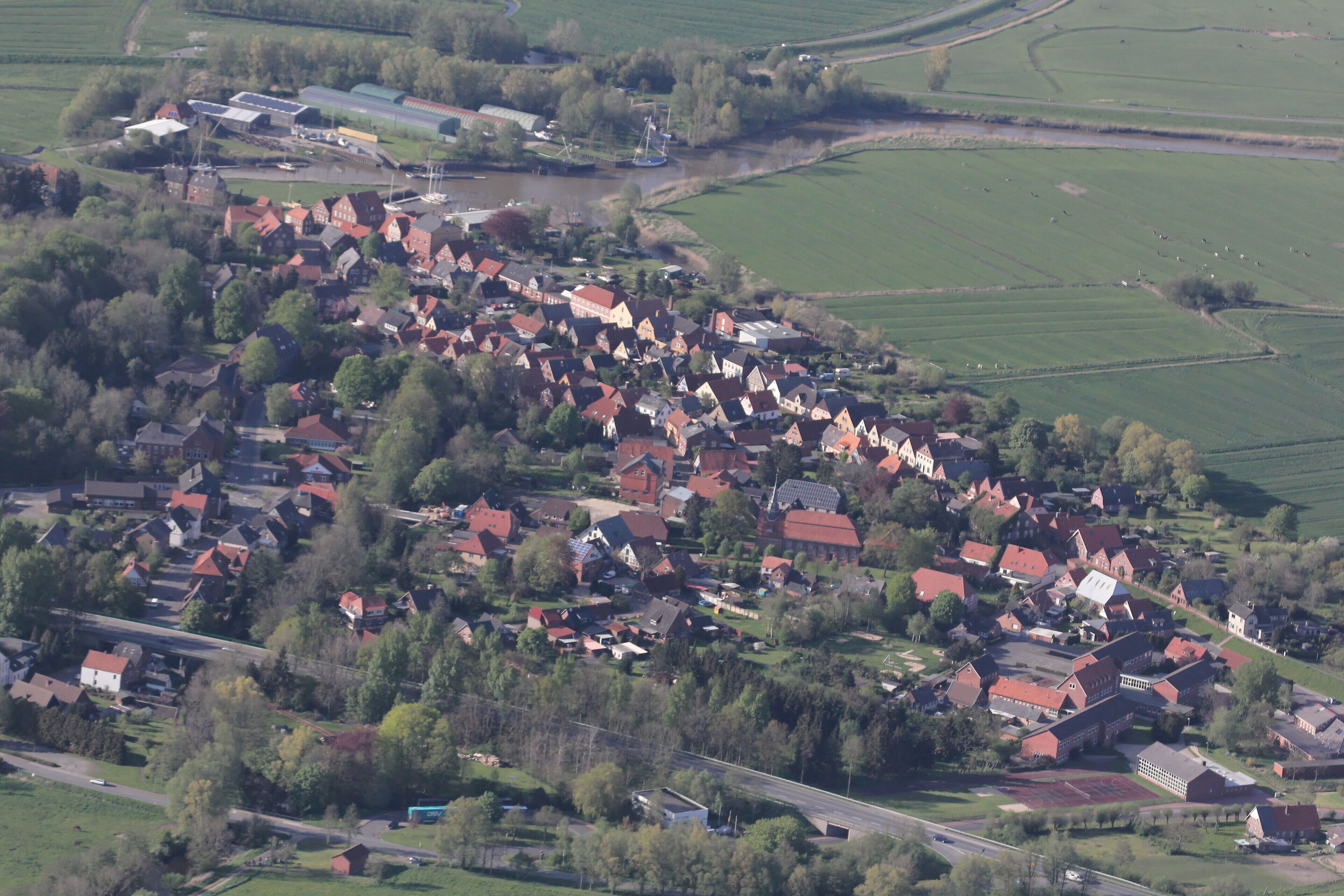 An aerial view of a rural village with red-roofed houses, green fields, and a river.