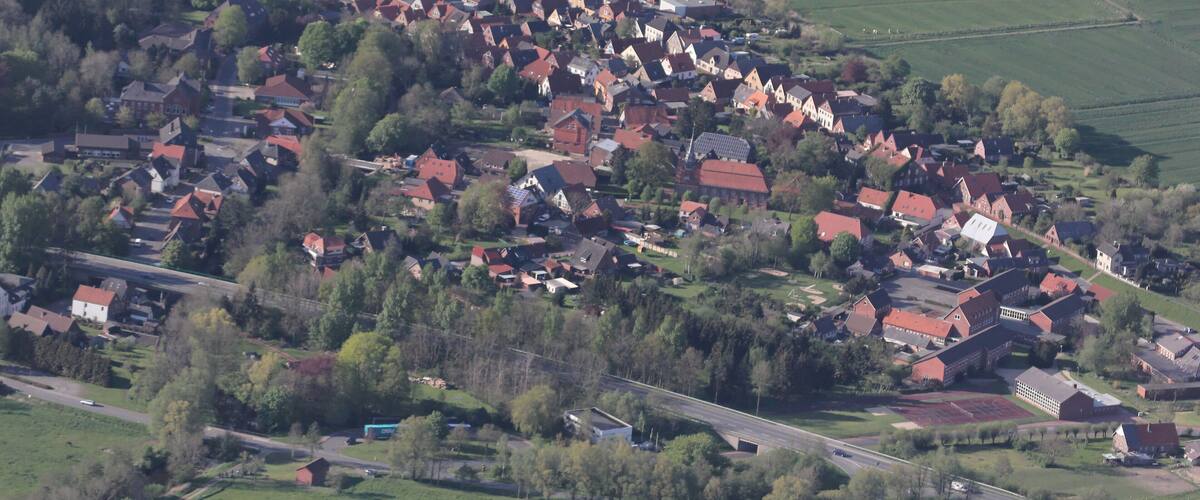 An aerial view of a rural village with red-roofed houses, green fields, and a river.