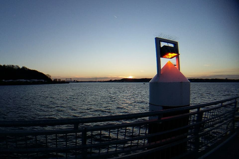 Um pôr do sol sobre a água, com um farol em primeiro plano.