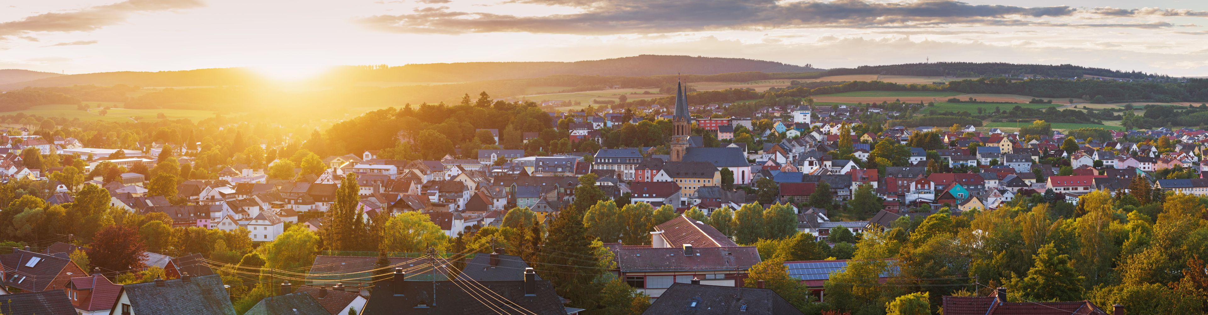 A town with a prominent church steeple, surrounded by residential houses and lush greenery.