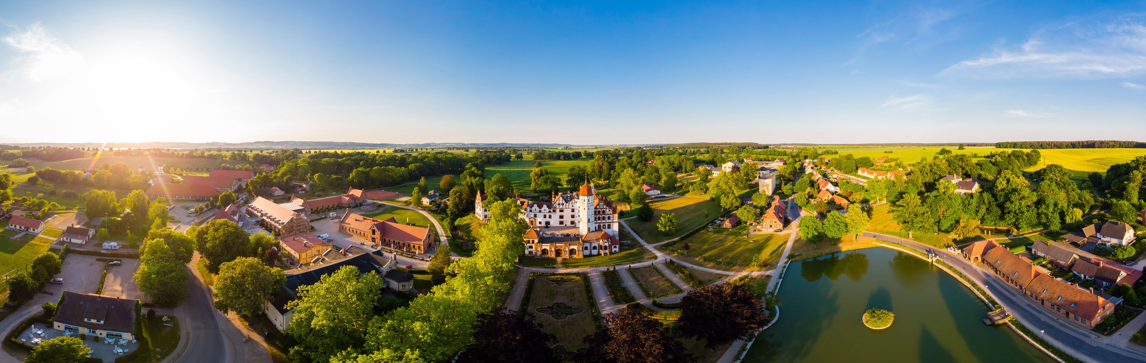 An aerial view of a historic town with a prominent castle, a river, and surrounding green fields.