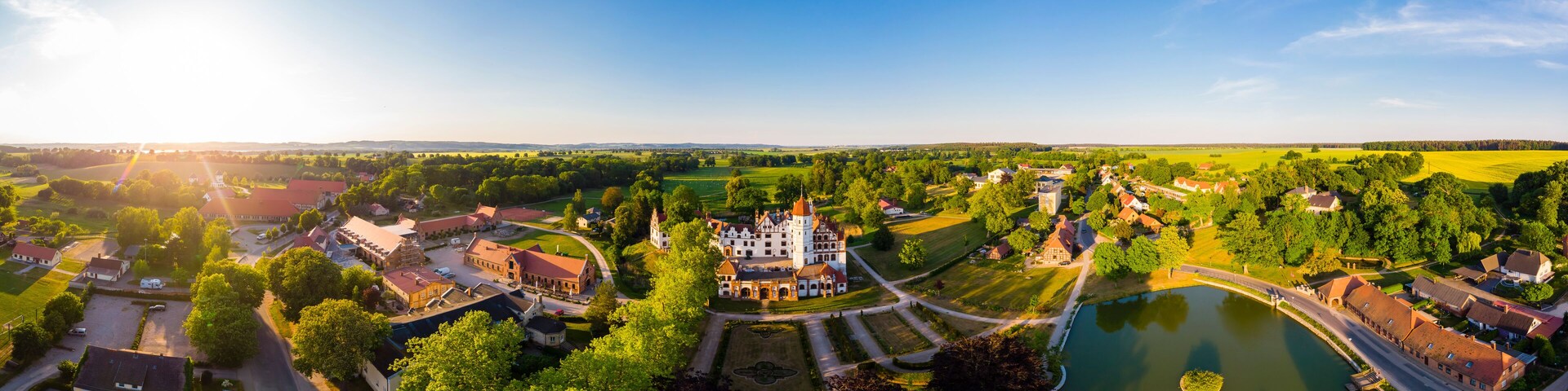 An aerial view of a historic town with a prominent castle, a river, and surrounding green fields.