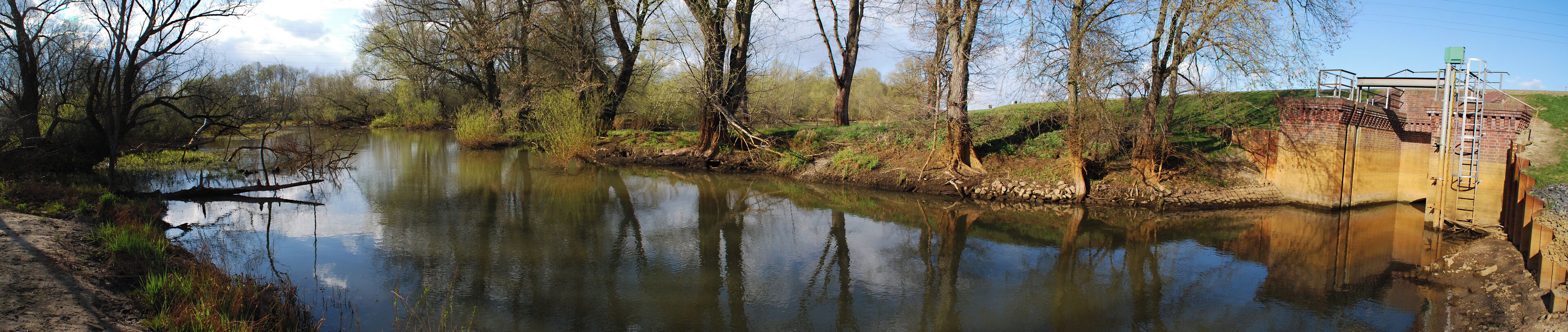 A calm river with reflections of trees and a bridge with a ladder.