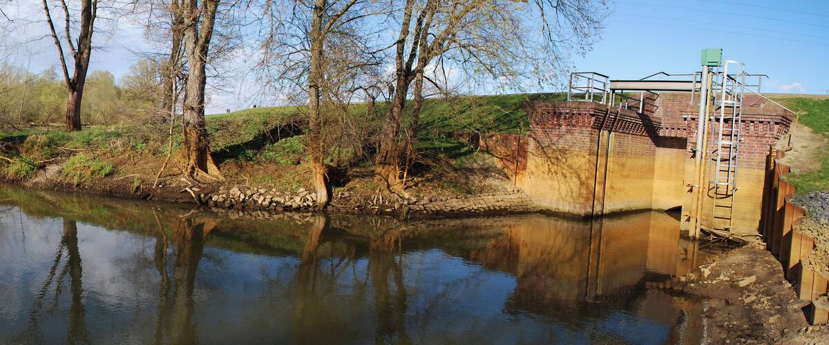 A calm river with reflections of trees and a bridge with a ladder.