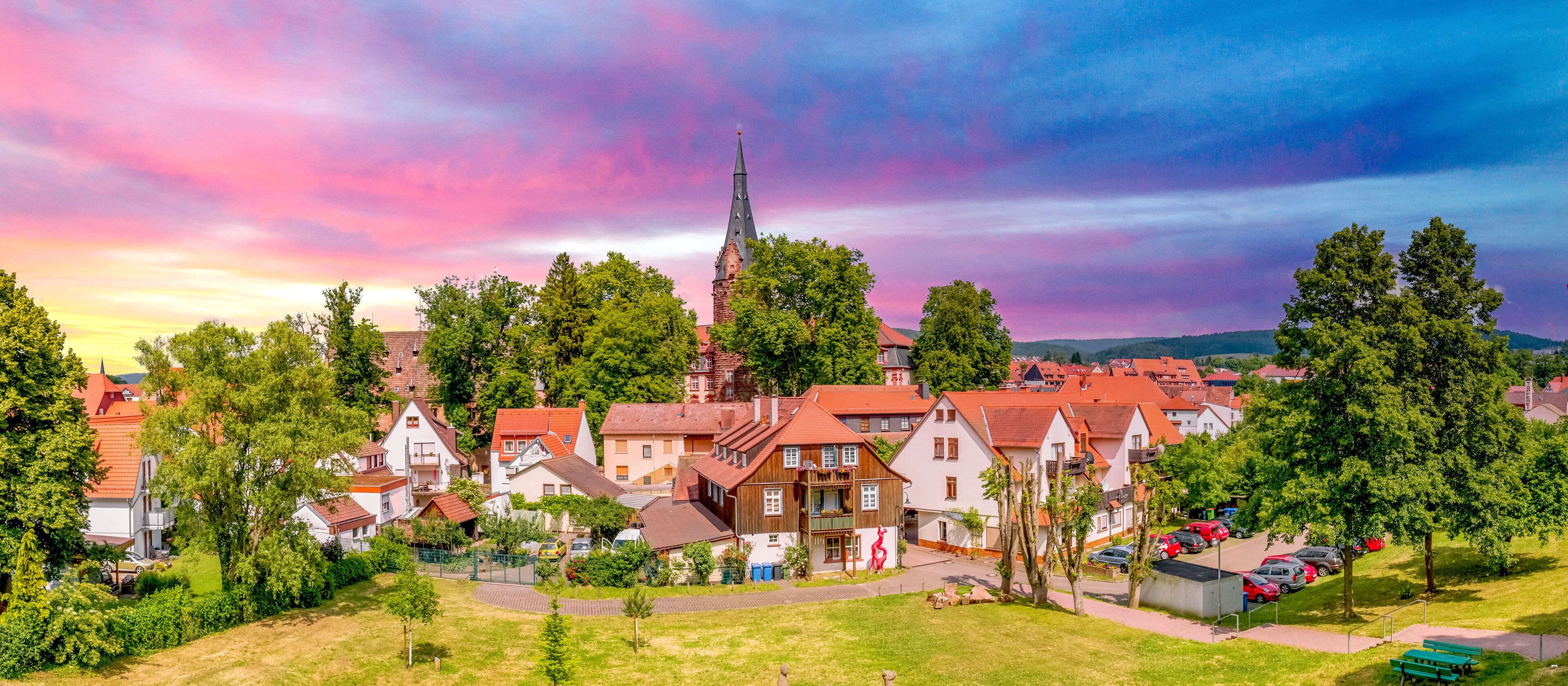 A town with red-roofed houses, a church with a tall spire, and a park with benches.