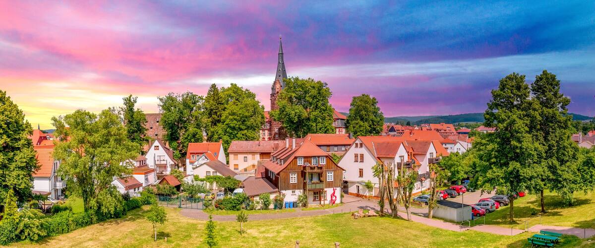 A town with red-roofed houses, a church with a tall spire, and a park with benches.