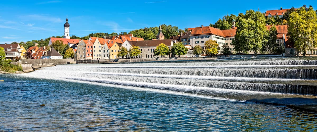 A river with a multi-tiered waterfall, historic buildings, and a church tower.