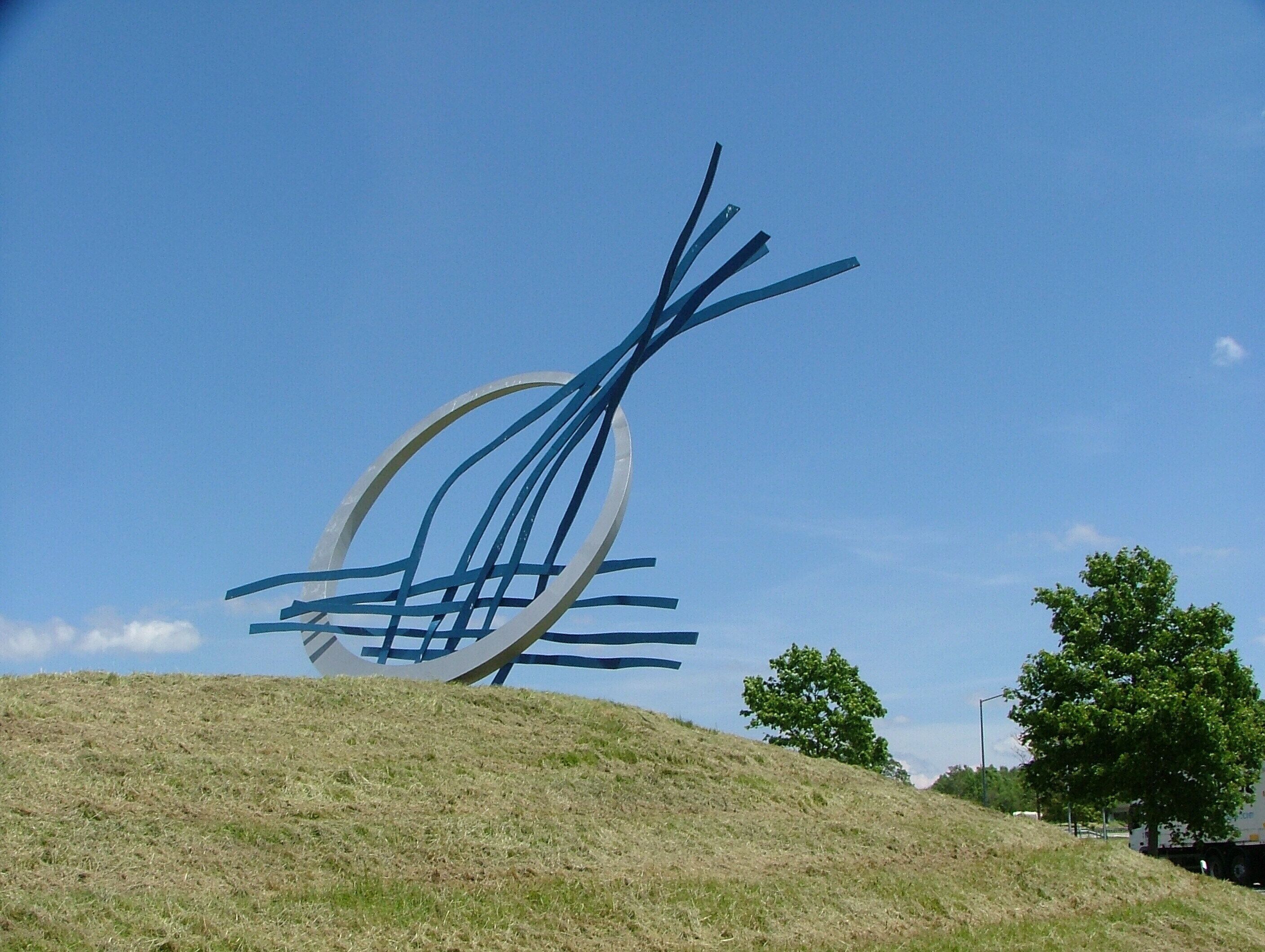 A metal sculpture on a grassy hill with a clear blue sky.