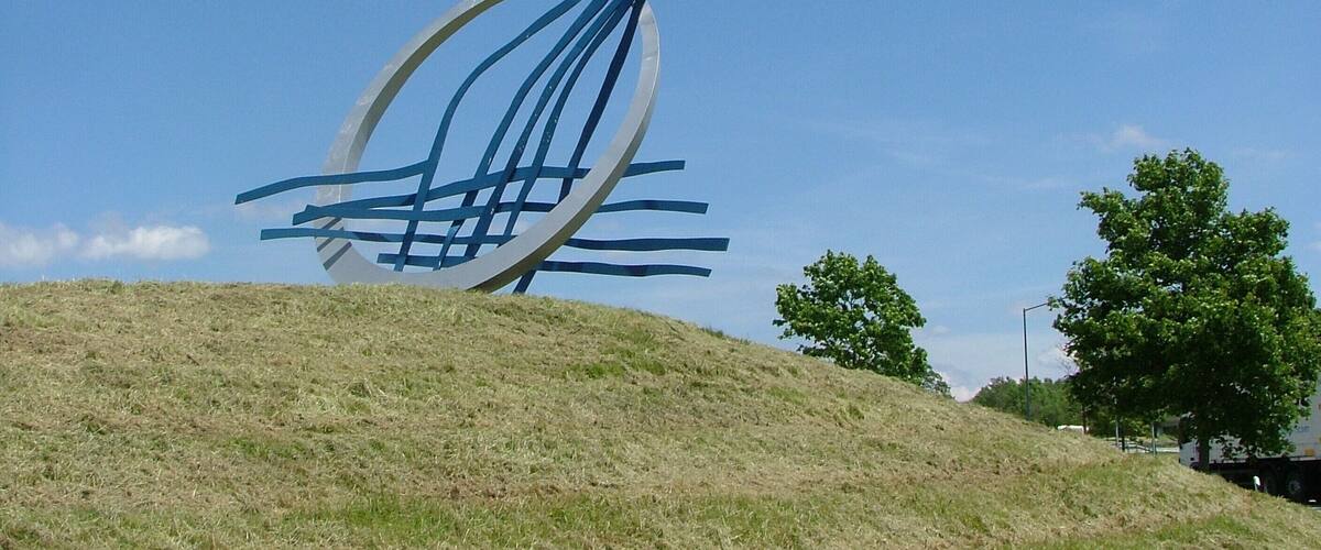 A metal sculpture on a grassy hill with a clear blue sky.