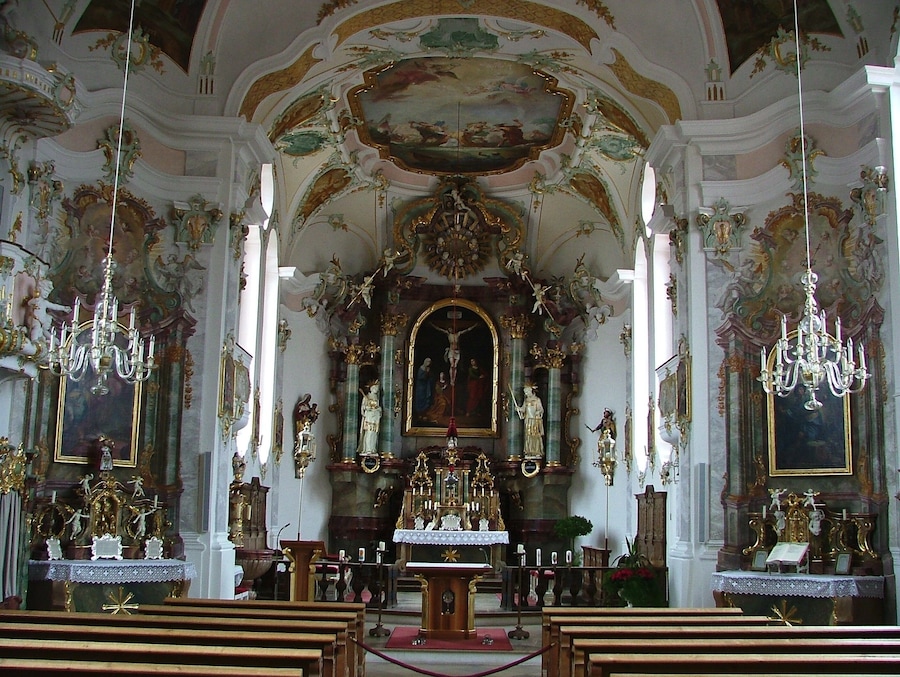 An ornate church interior with elaborate ceiling frescoes, gilded altars, and chandeliers.
