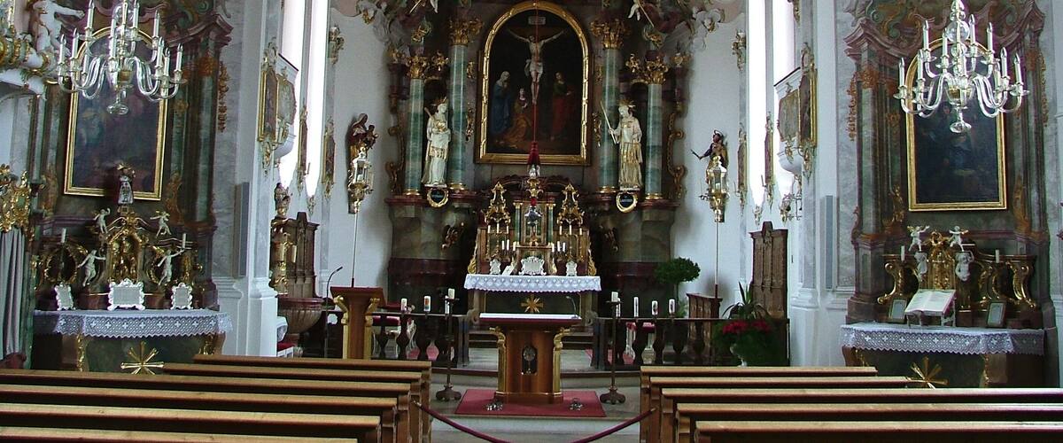 An ornate church interior with elaborate ceiling frescoes, gilded altars, and chandeliers.