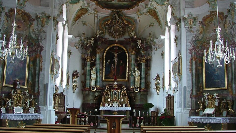An ornate church interior with a central altar, religious statues, and elaborate ceiling frescoes.