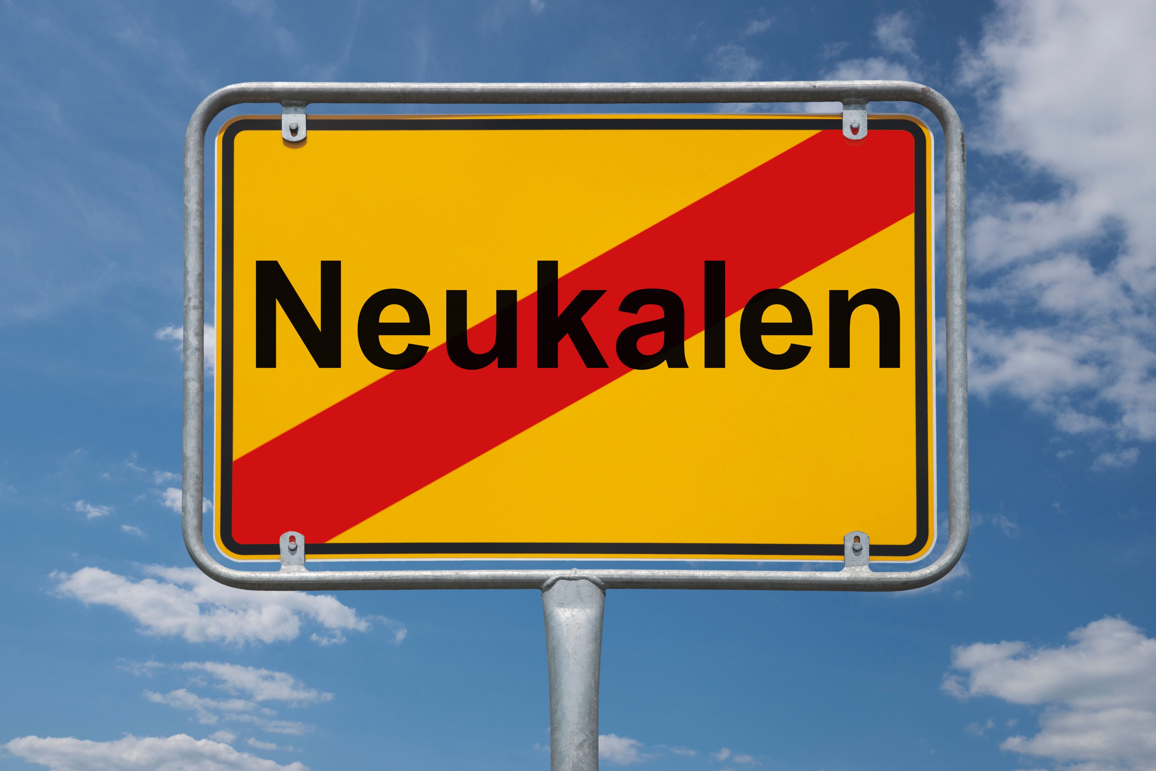 Placa de rua com a palavra 'Neukalen' sob um céu azul com nuvens.
