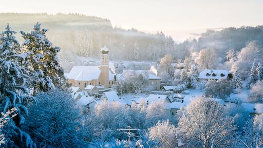 Un pueblo cubierto de nieve con una iglesia, casas y árboles.