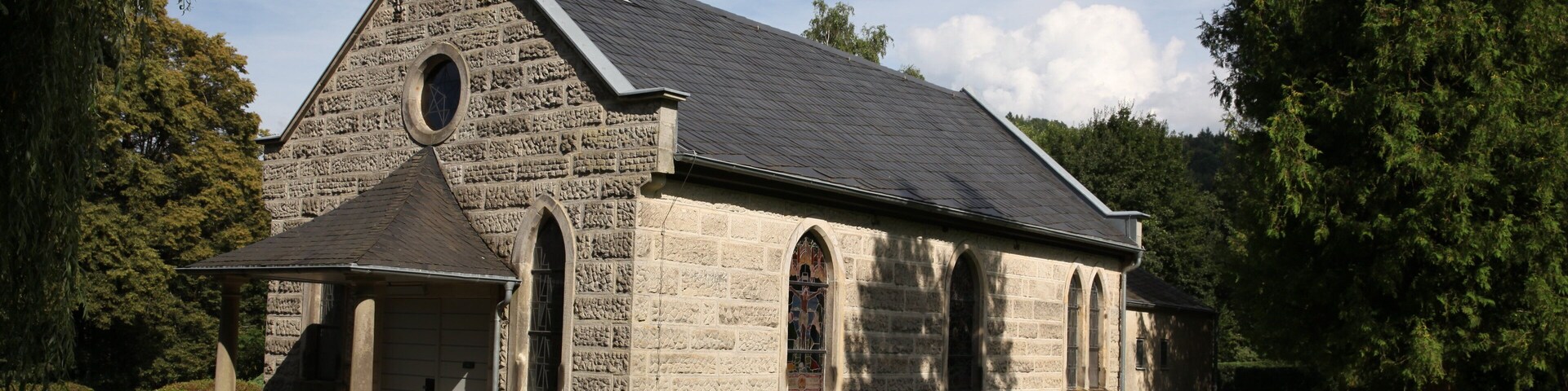 A stone church with a steep gable roof and a cross on top.