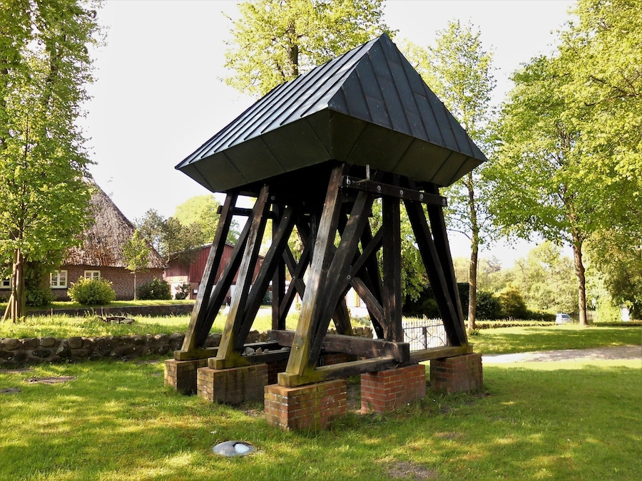 A wooden gazebo with a sloped roof in a park.
