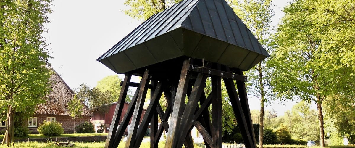 A wooden gazebo with a sloped roof in a park.
