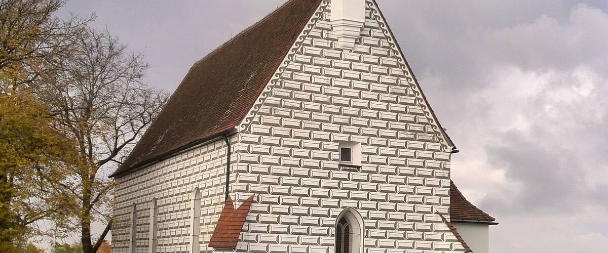 A white church with a brick pattern, a bell tower, and a steep roof.