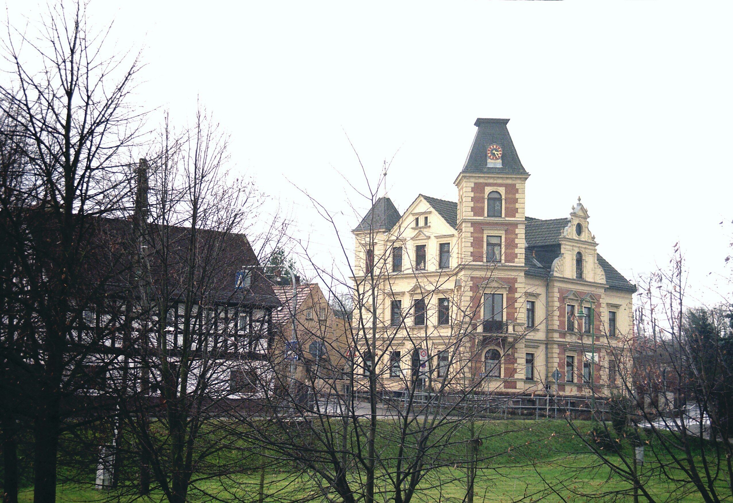 A large, historic building with a clock tower, surrounded by trees and a grassy area.