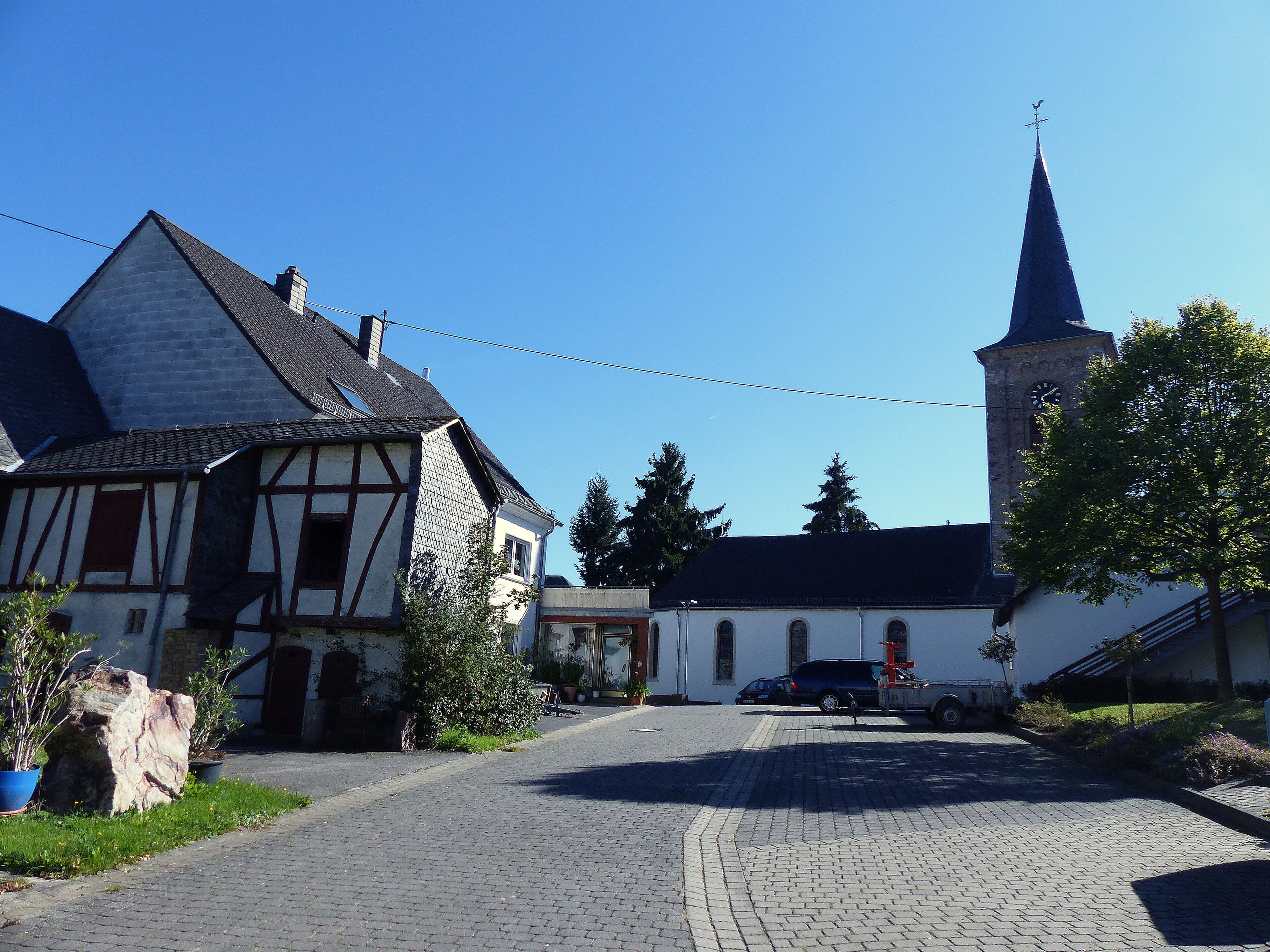A cobblestone street, a church with a clock tower, and traditional half-timbered houses.