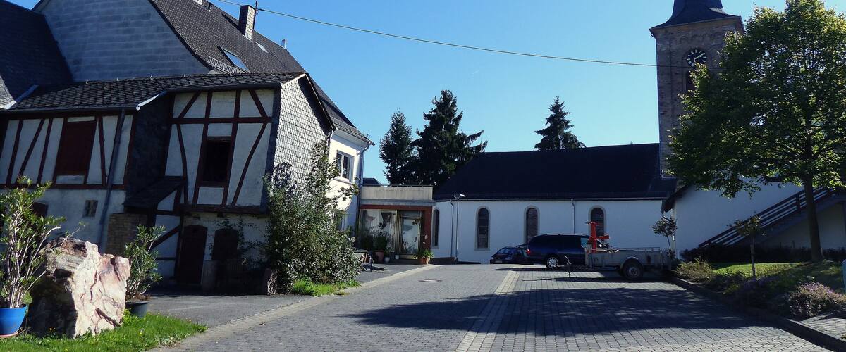 A cobblestone street, a church with a clock tower, and traditional half-timbered houses.