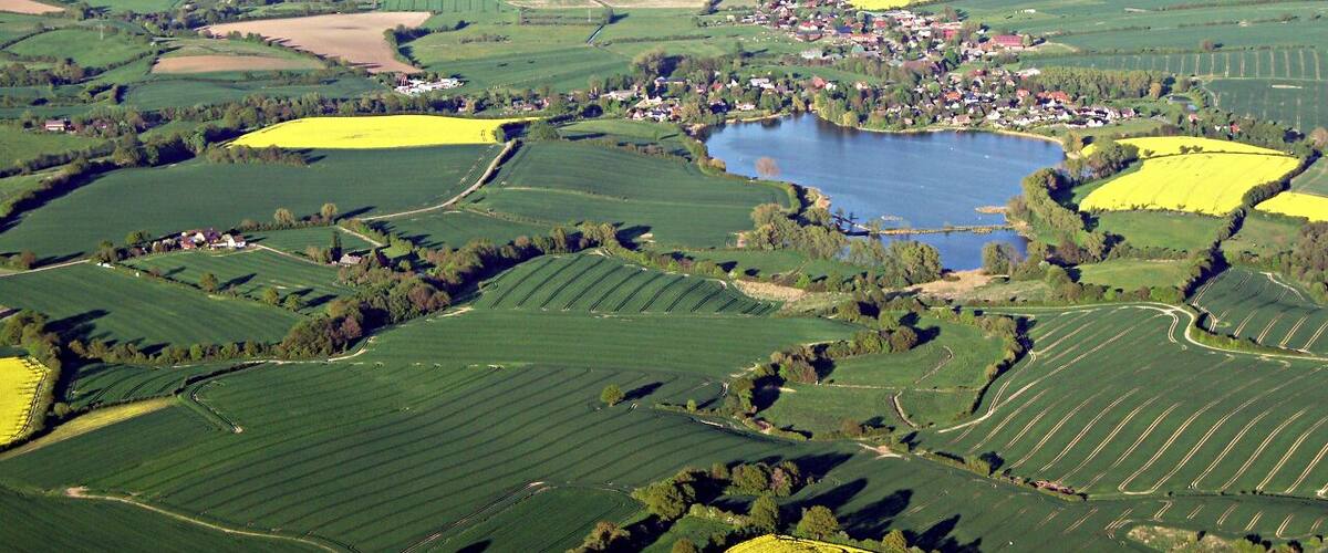An aerial view of a rural landscape with fields, a small town, and a lake.