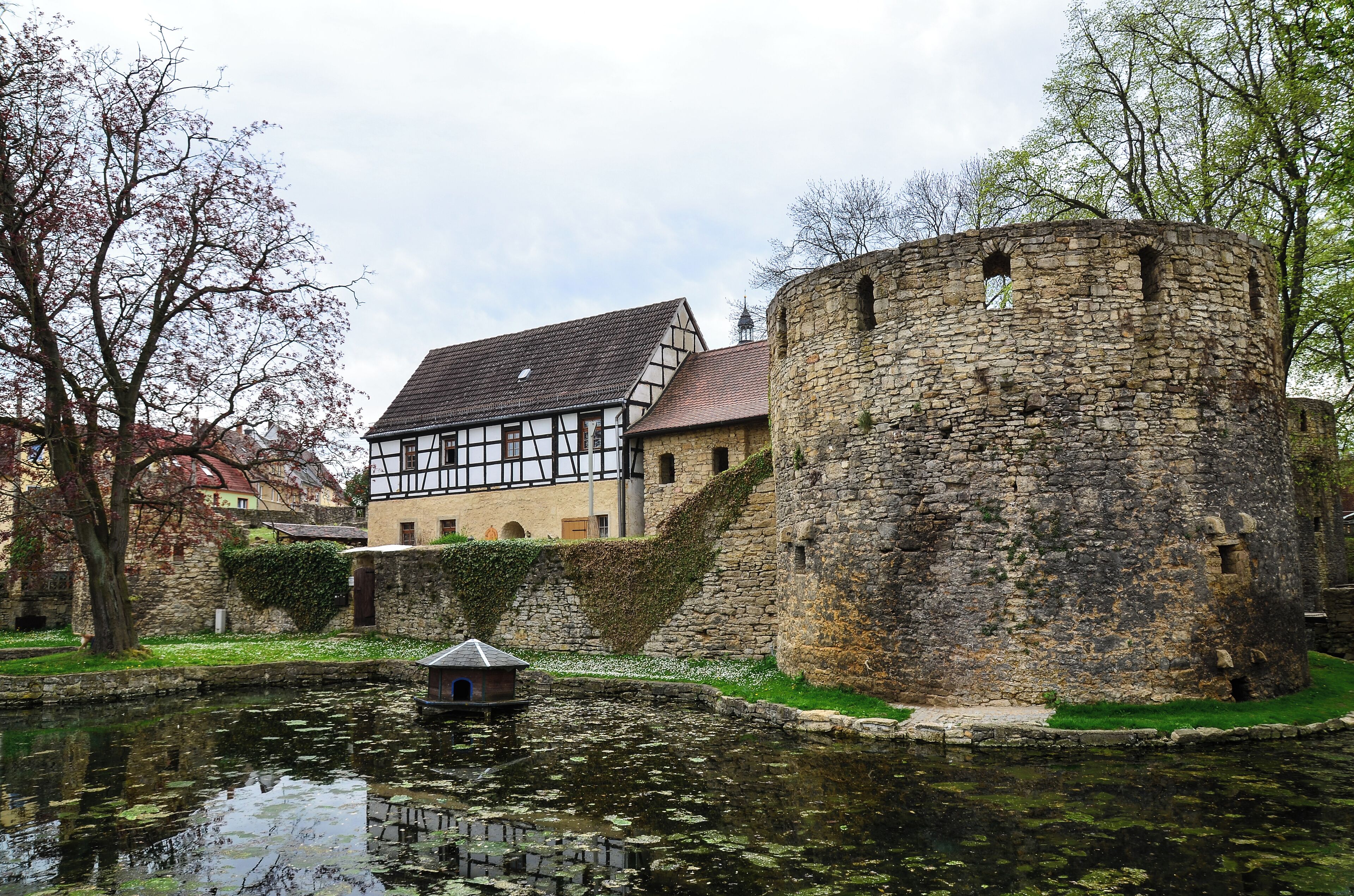 A historic building with a stone tower and a half-timbered house by a canal.