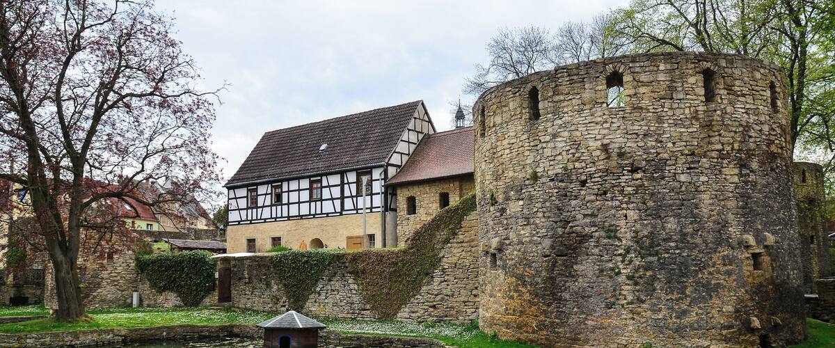 A historic building with a stone tower and a half-timbered house by a canal.