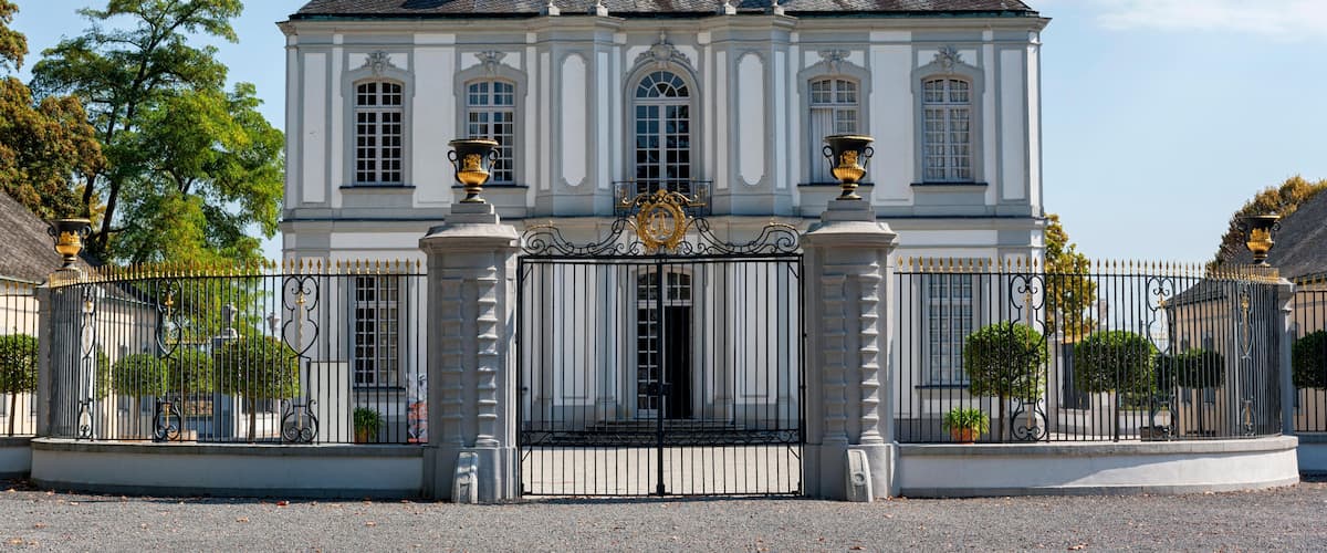 A grand white building with a black iron gate, topped with a golden emblem.