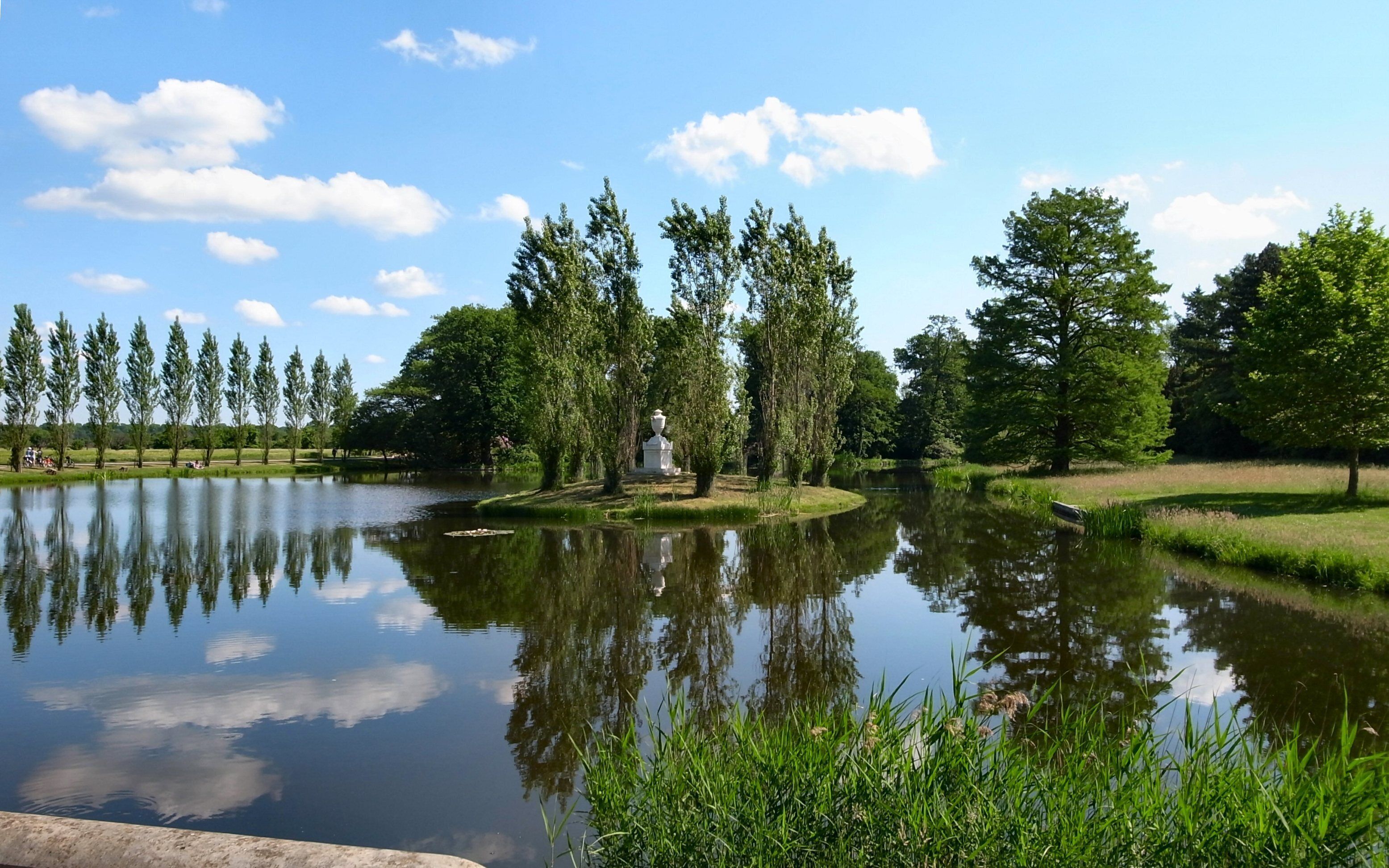 A calm lake with reflections of trees and a white statue in the center.