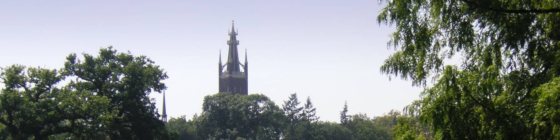 A calm lake with a boat carrying people, surrounded by lush greenery and a distant church tower.