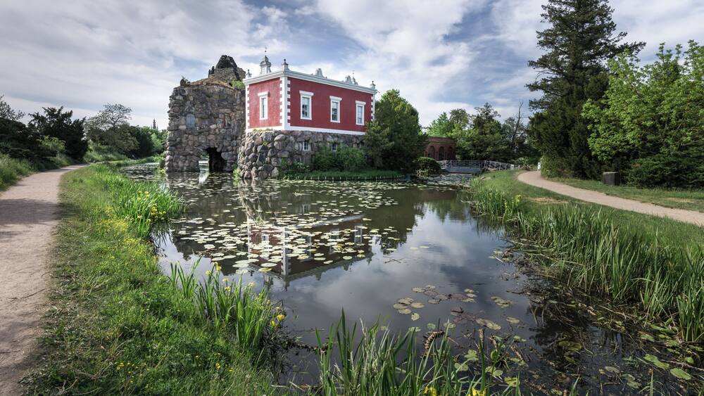 A historic building with a stone archway, a pond with lily pads, and a pathway.