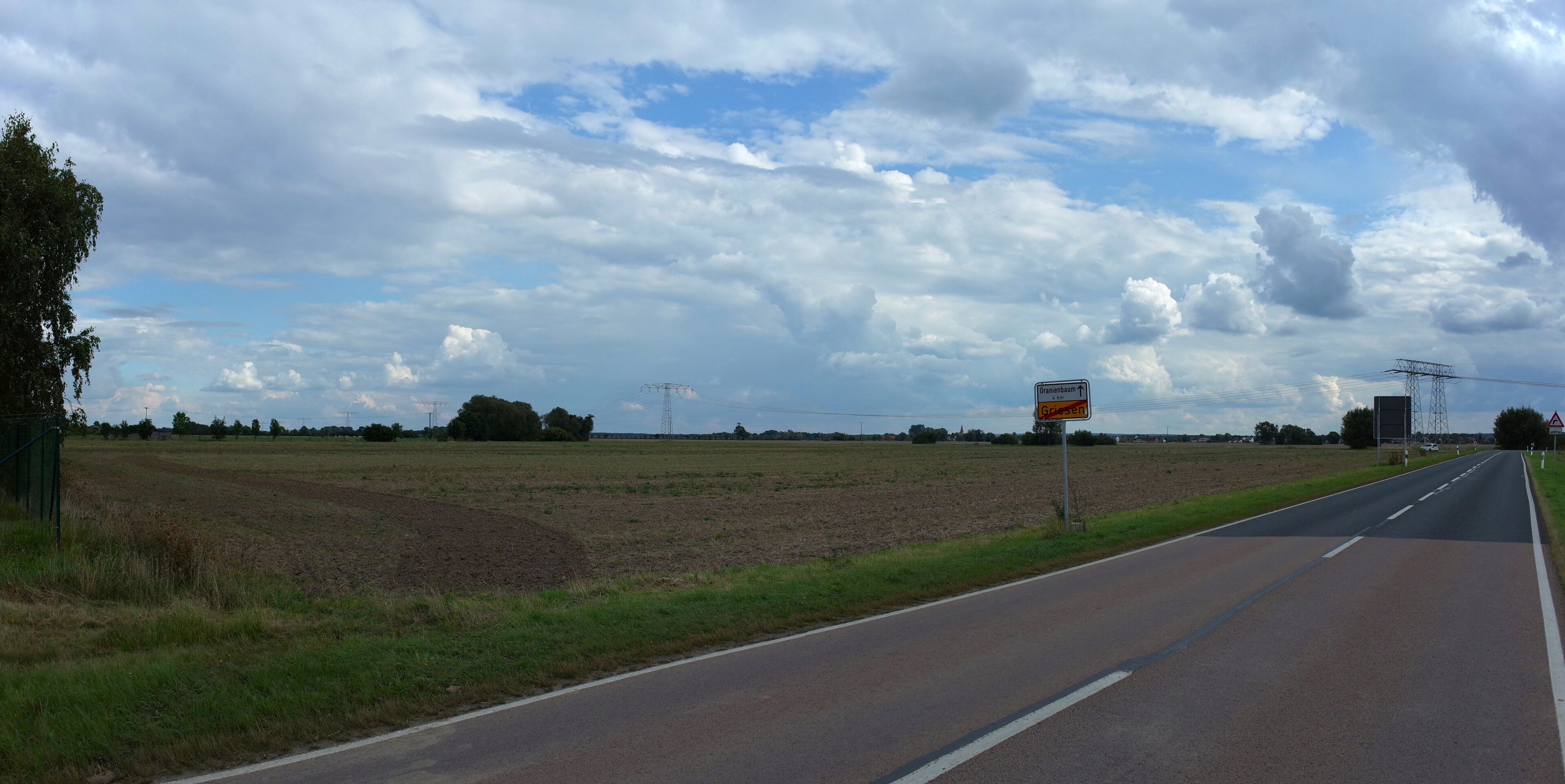 A rural road with fields on either side, a clear sky, and a directional sign for Griesheim.