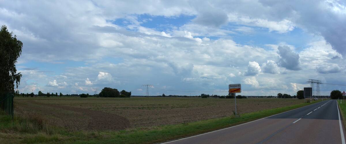 A rural road with fields on either side, a clear sky, and a directional sign for Griesheim.