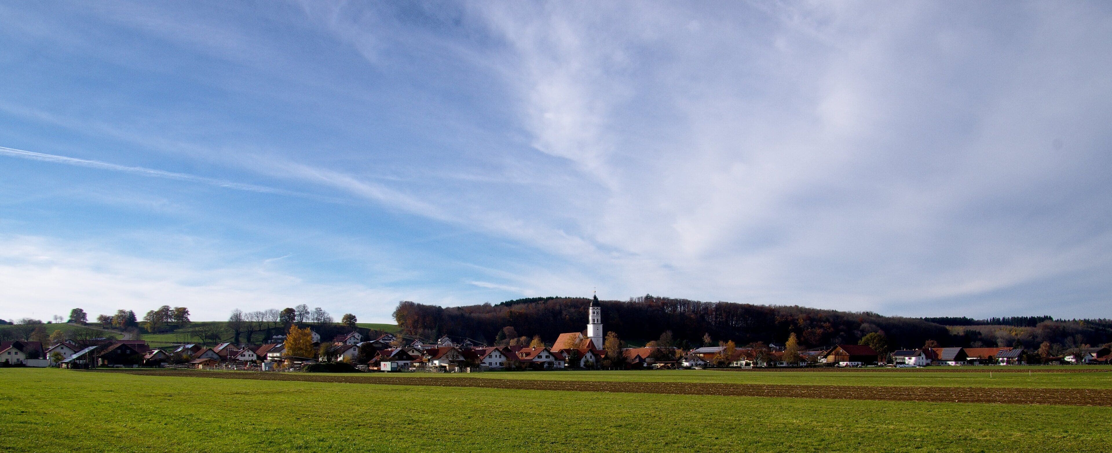 A village with a prominent church tower, surrounded by houses and fields.