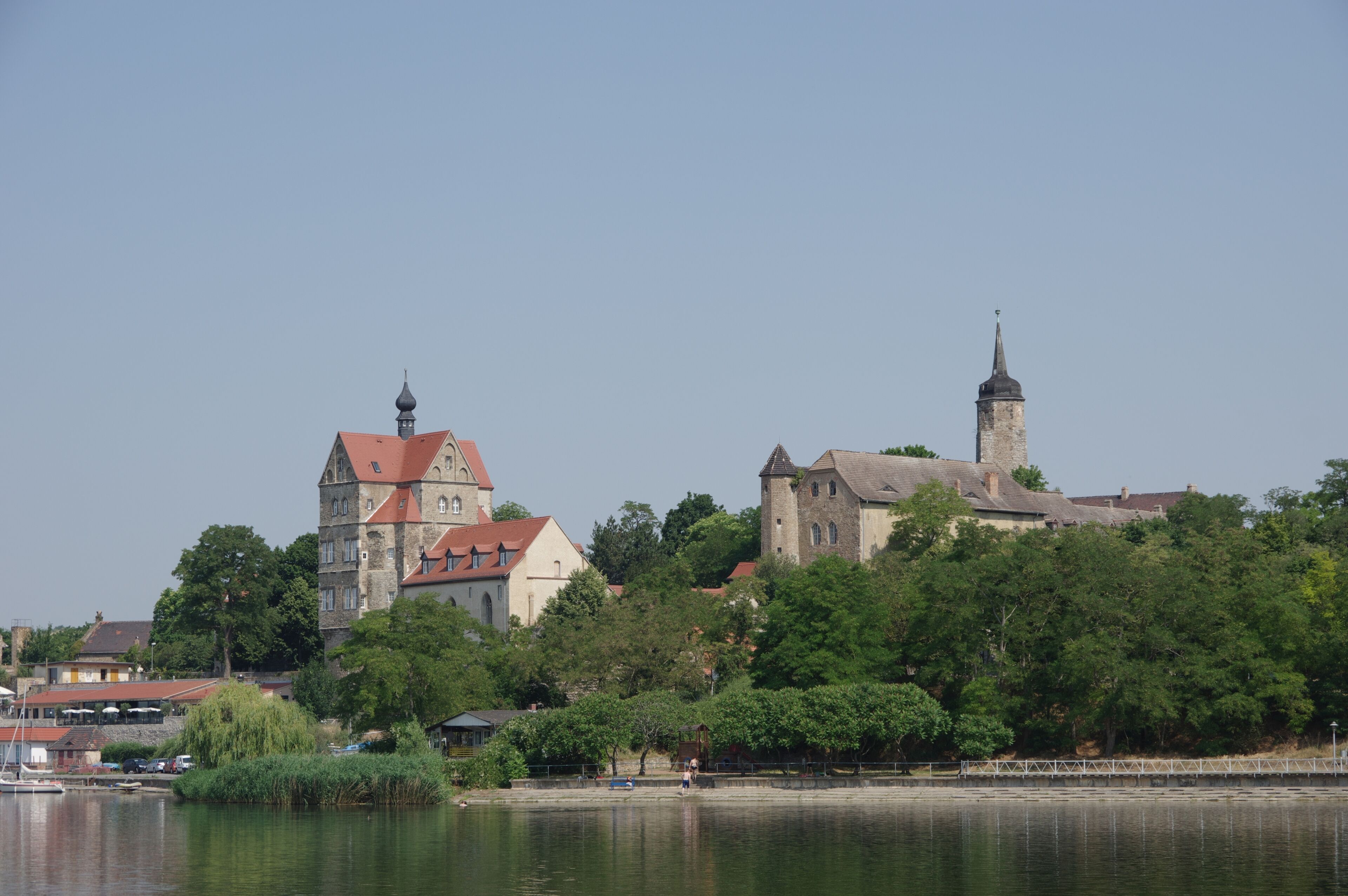 A riverside town with historic buildings, including a church with a tower and a castle-like structure.