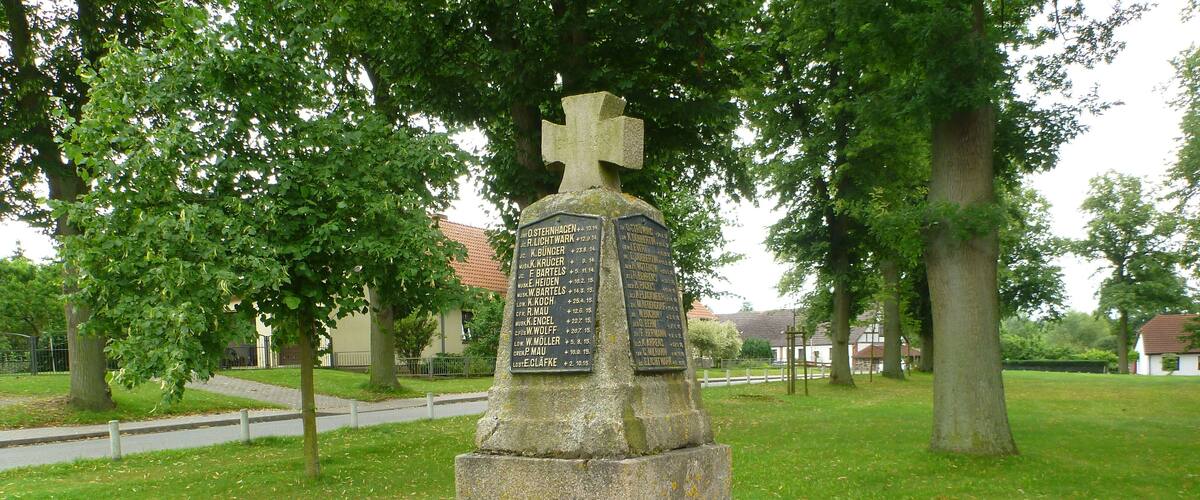 A stone monument with inscriptions, surrounded by grass and trees in a park.