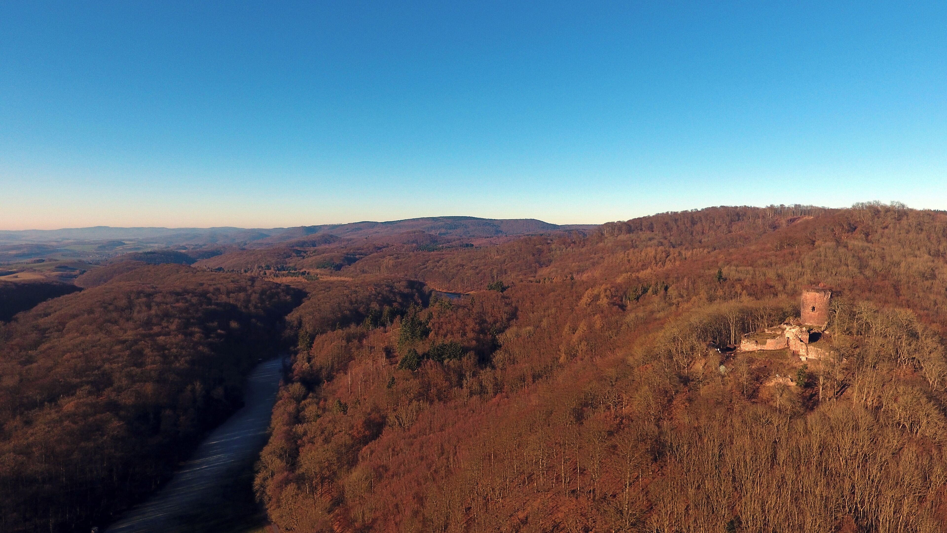 A river winding through a forested valley with a small, isolated structure on a hill.