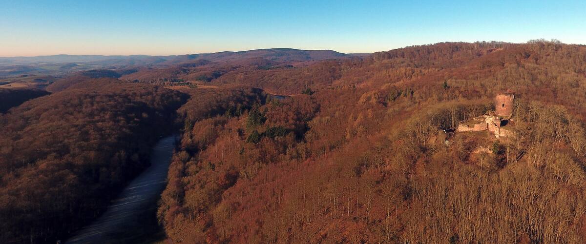 A river winding through a forested valley with a small, isolated structure on a hill.