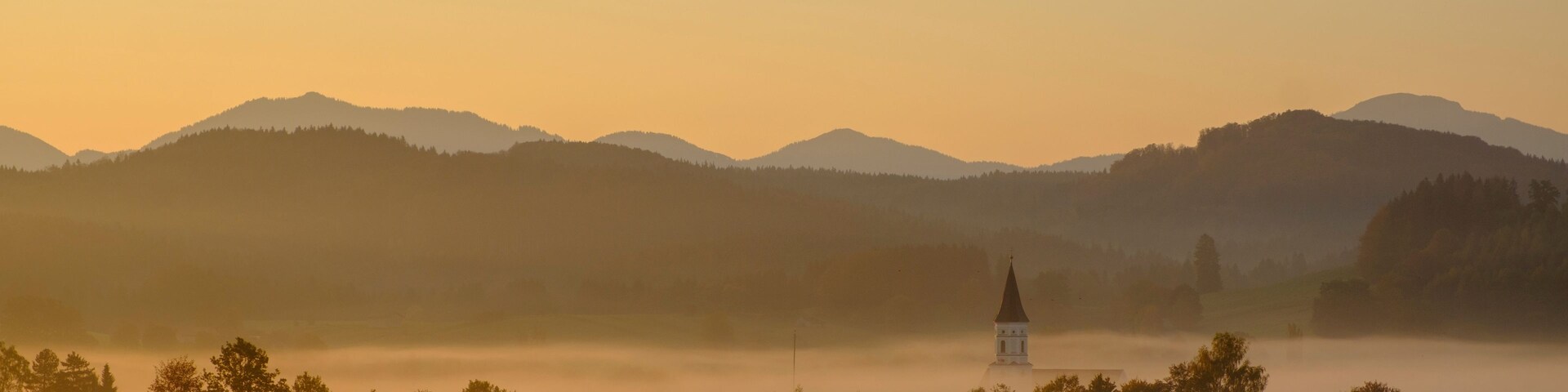Eine Kirche, umgeben von nebelverhangenen Hügeln und einem Sonnenaufgang.