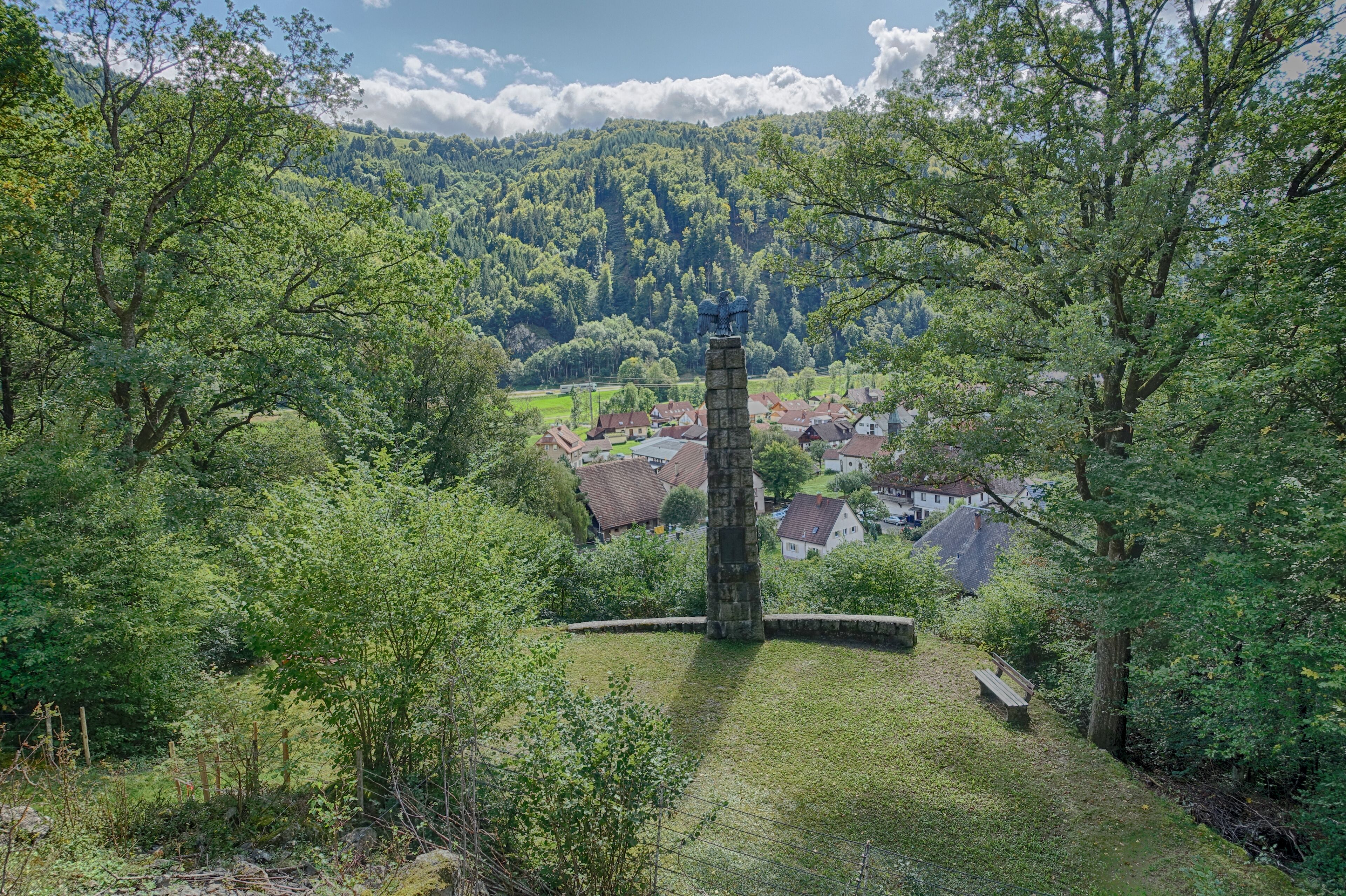 A stone tower in a lush green valley with a village in the background.