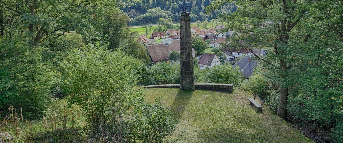 A stone tower in a lush green valley with a village in the background.