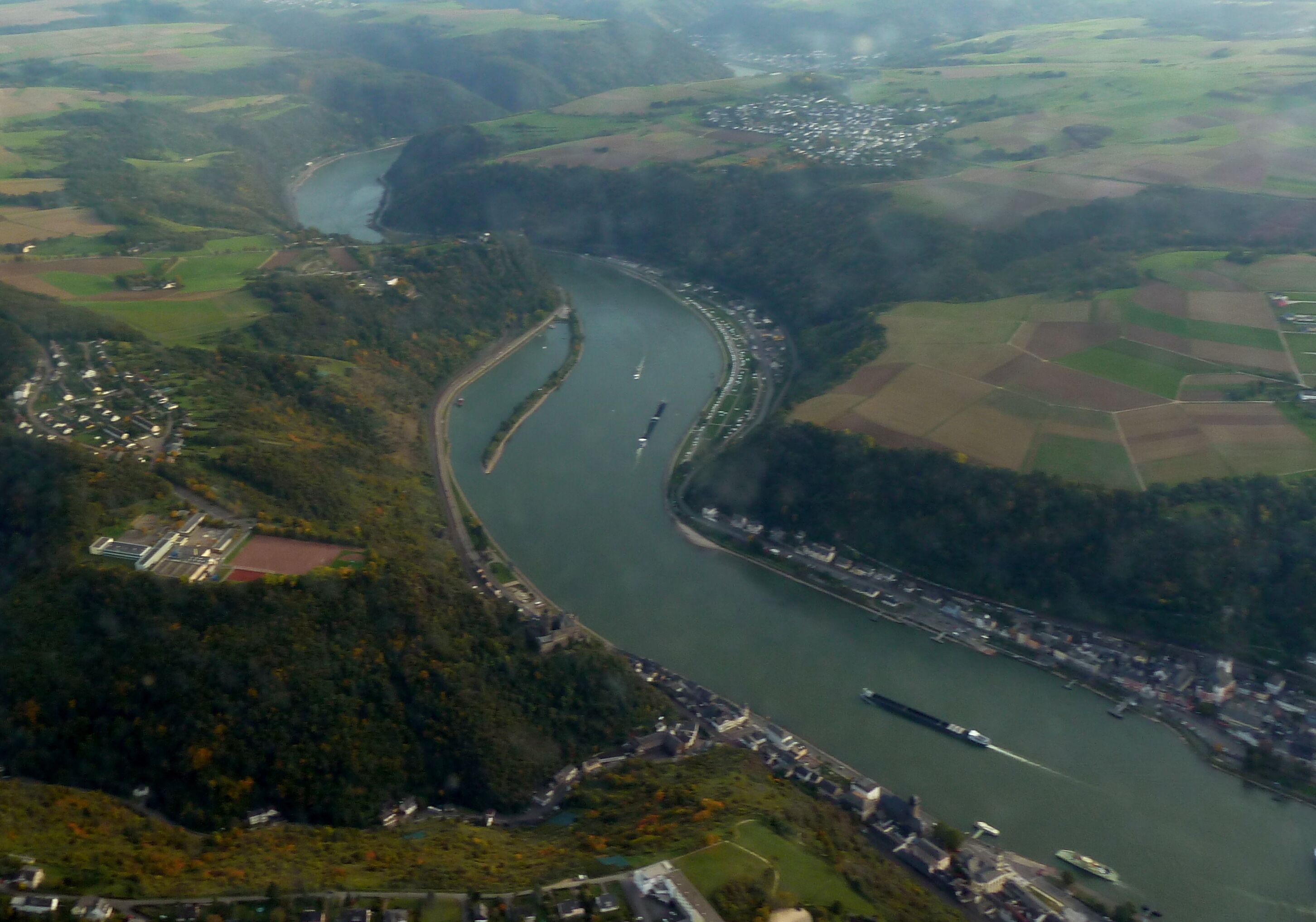 An aerial view of a river winding through a town surrounded by green fields and hills.