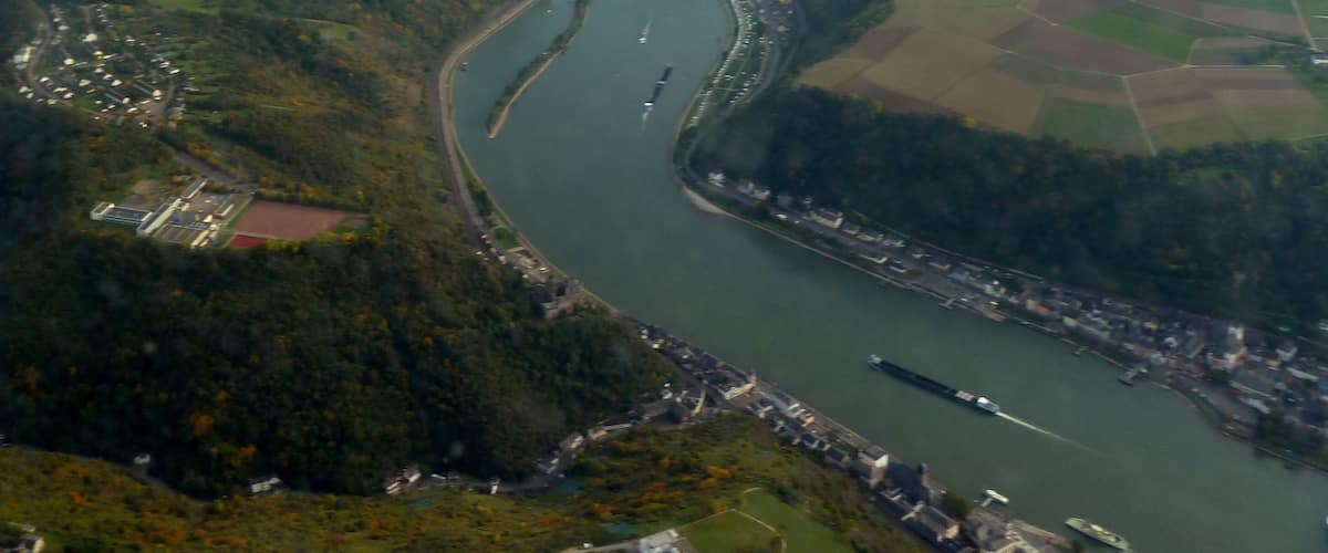 An aerial view of a river winding through a town surrounded by green fields and hills.