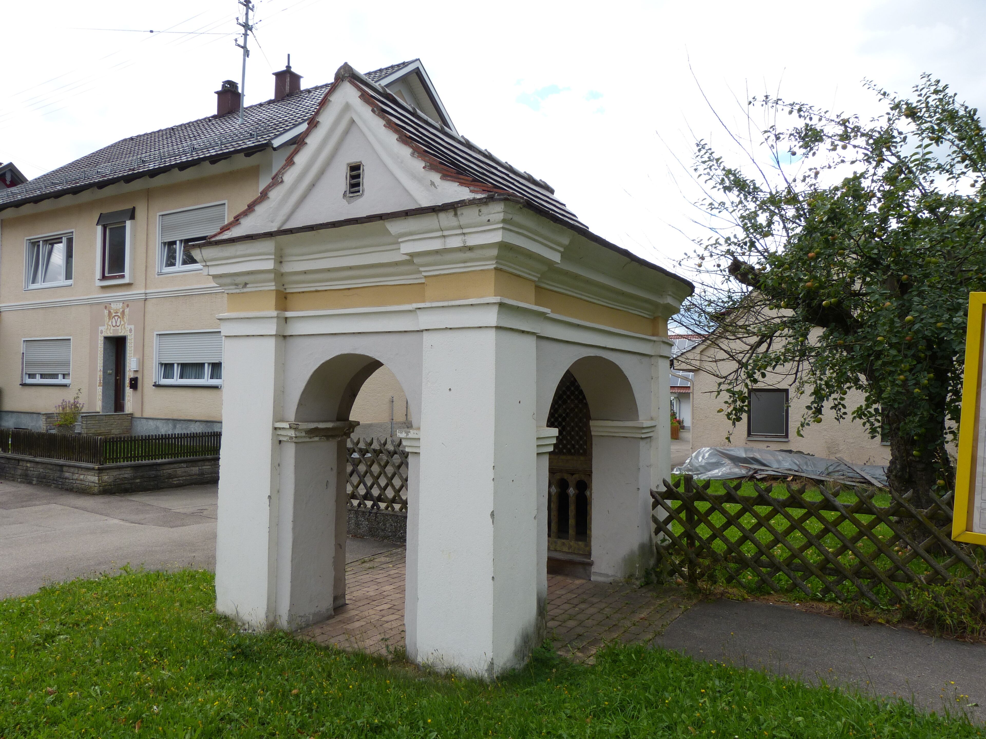 A white gazebo with arches, a tiled roof, and a yellow fence in a residential area.