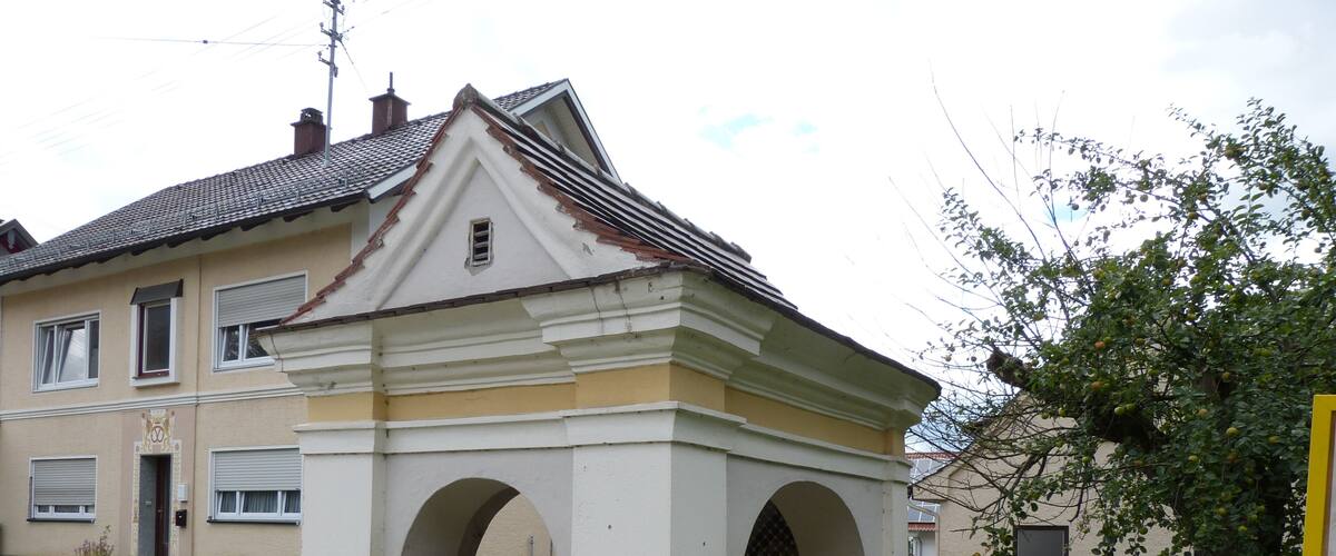A white gazebo with arches, a tiled roof, and a yellow fence in a residential area.