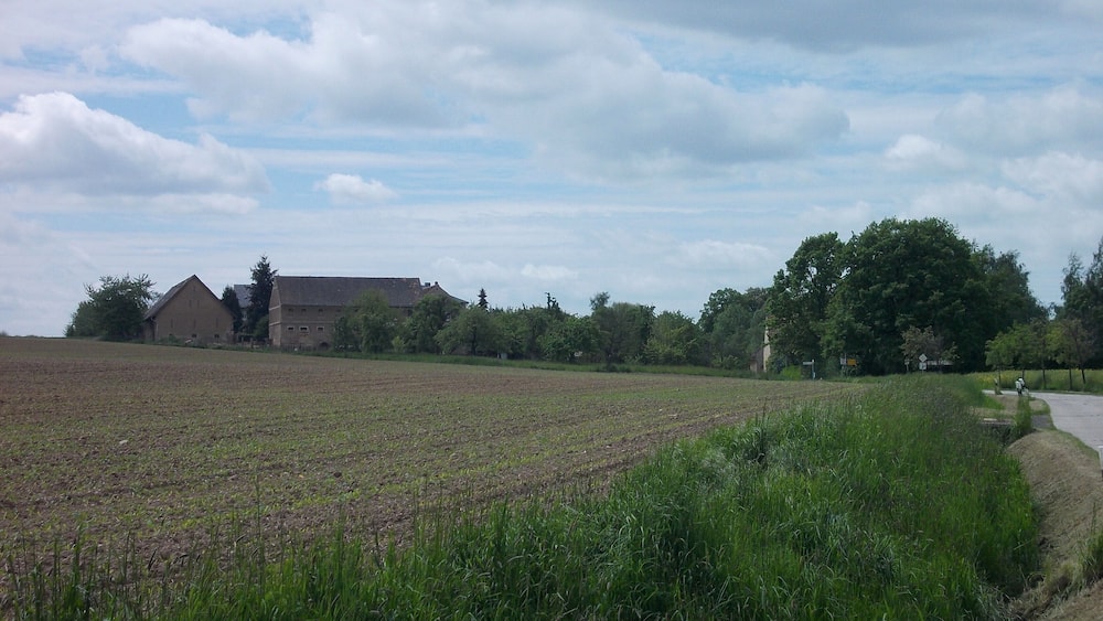 Un paysage rural avec un grand champ, une grange et une route qui serpente à travers le champ.