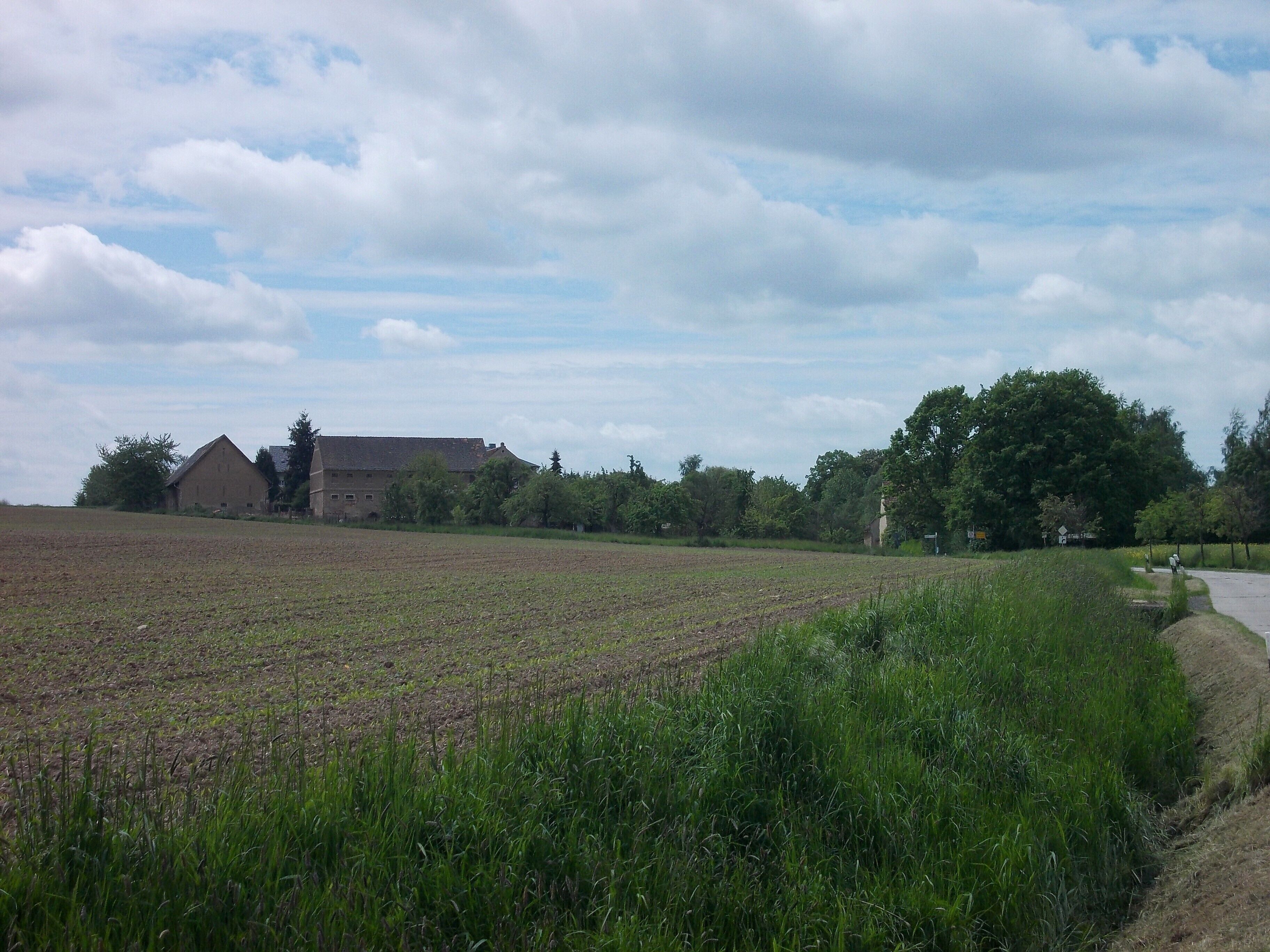 A rural landscape with a large field, a barn, and a road curving through the field.