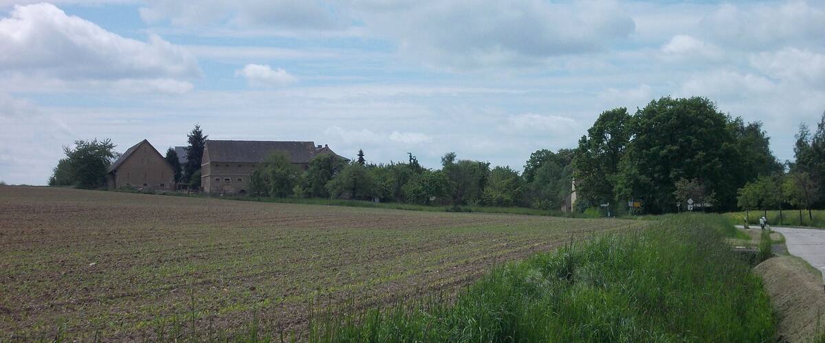 A rural landscape with a large field, a barn, and a road curving through the field.