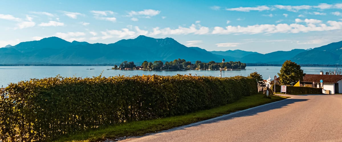A lake with mountains in the background, a road, and a small island with buildings.